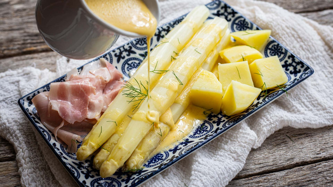 Weisser Spargel mit Salzkartoffeln und Sauce Hollandaise auf einem eckigen, blau-gemusterten Teller